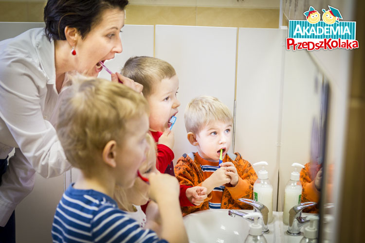 Dzieci razem z panią dentyską fluoryzują ząbki. W łazience, przed lustrem.