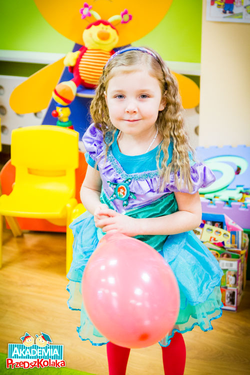 Przedszkolaczka przebrna za księżniczkę. Piękna turkusowa suknia. Dzieczynka stoi z balonem w ręku.
