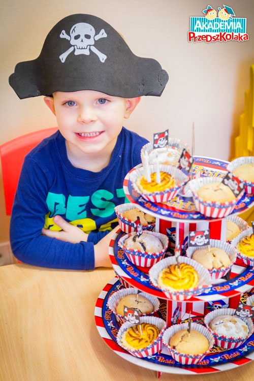 Przedszkolak obchodzi urodziny. Siedzi w czapce pirata, przed talerzmi z pysznymi babeczkami
