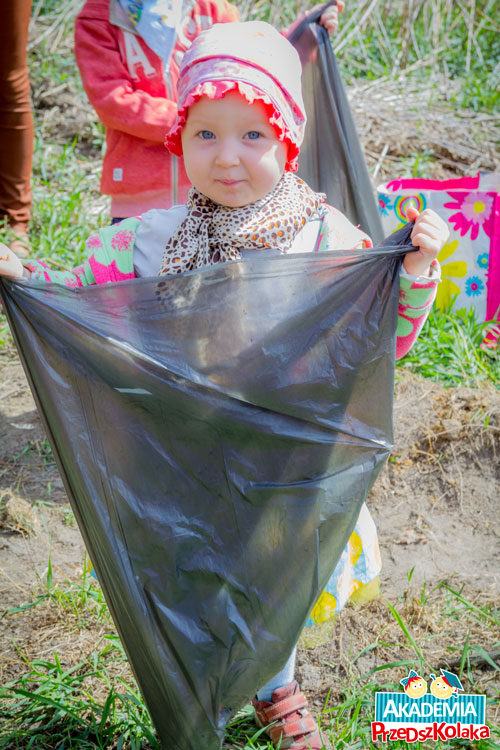 Dziewczynka trzyma worek na śmieci. W lasku dzieci zbierają śmieci w ramach Tygodnia Ziemi.