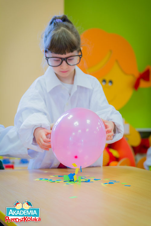 Przedszkolak naelektryzowanym balonem podnosi kawałki papieru ze stolika.