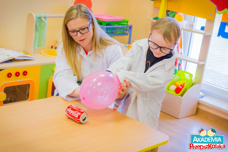 Przedszkolak z pomocą Cioci, naelektryzowanym balonem przesuwa puszkę po stoliku.