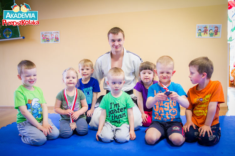 Zdjęcie naszego trenera Staśka razem z przedszkolakami. Dwoje dzieci trzyma medale.