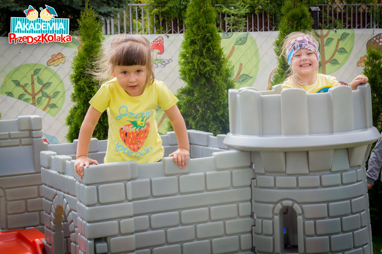 Dwie dziewczynki bawią się w plastikowym zamku na placu zabaw.