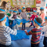 Przedszkolaki stoją w kółku. Zabawa ruchowa przy użyciu niebieskiej folii.