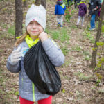 Zdjęcie przedszkolaka w lesie. Dziecko trzyma worek na śmieci.
