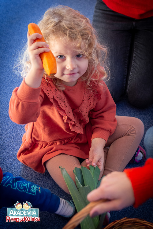 Przedszkolanka pokazuje obraną marchewkę, którą wyczuła dotykiem wśród innych warzyw.