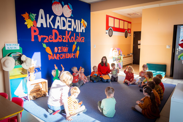 Sala przedszkolna w przedszkolu Akademia Przedszkolaka na Białołęce. Dzieci z nauczycielkami siedzą w kółku na dywanie.