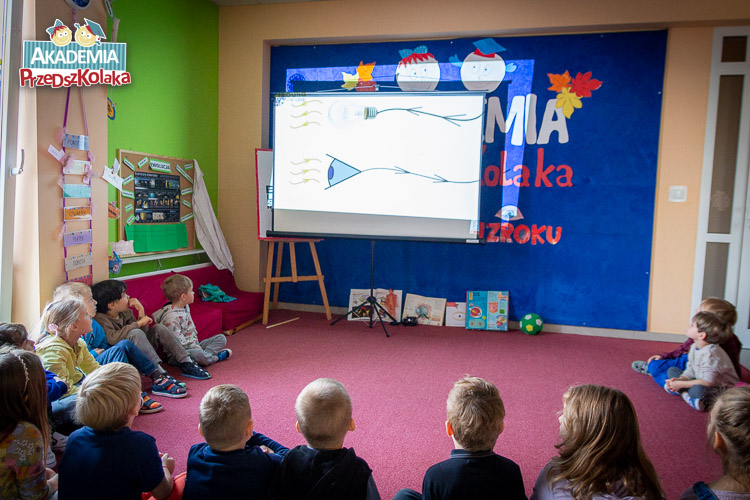 Przedszkolaki siedzą na dywanie w sali przedszkolne, w przedszkolu na Białołęce. Na ekranie wyświetlany jest film. Na uchwyconym kadrze widzimy oczy.