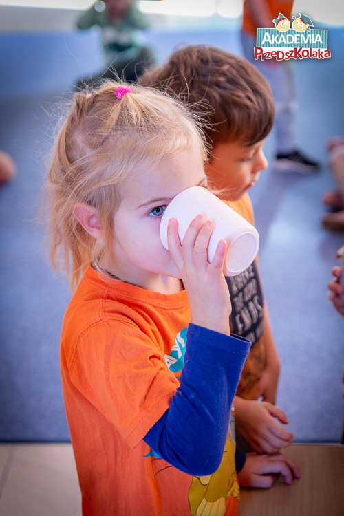 Przedszkolanka pije z białego kubka sok warzywno owocowy przygotowany wspólnymi siłami.