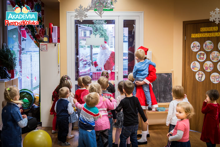 Dzieci w drzwiach, wszystkie razem,  witają Świętego Mikołaja. 