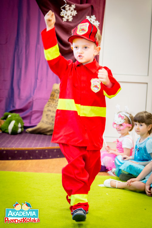 Przedszkolak w stroju strażaka. Ma mundur i czapkę w kolorze czerwonym
