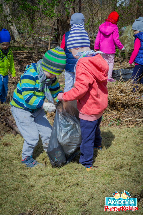 Chłopiec trzyma worek na śmieci a drugi wrzuca do środka znalezione śmieci. W lasku dzieci zbierają śmieci w ramach Tygodnia Ziemi.