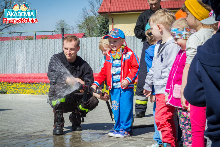 Kolejka przedszkolaków do lania wodą z węża strażackiego.