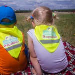 Dwoje przedszkolaków siedzących na trawie i obserwujących pas startowy.