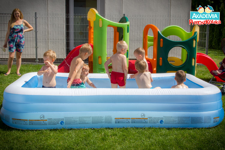 Przedszkolaki kąpią się w dmuchanym basenie postawionym w ogrodzie.