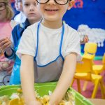 Uśmiechnięty przedszkolak miesza rękami piankę i farbki w kuwecie.