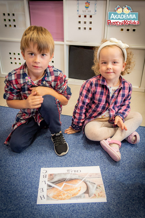 Zdjęcie dwójki przedszkolaków z ilustracją z puzzli przedstawiającą chleb. Obok podpis z literek ułożony w słowo CHLEB.