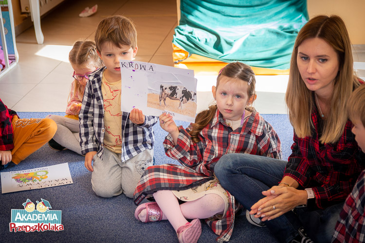 Chłopiec i dziewczynka z przedszkola na Białołęce trzymają przyklejone do kartki puzzle z obrazkiem krowy. Do kartki przyklejony jest także napis KROWA.