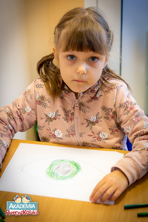 Kolejna przedszkolanka nad kartką papieru. Widać już piękne oko z zieloną źrenicą.